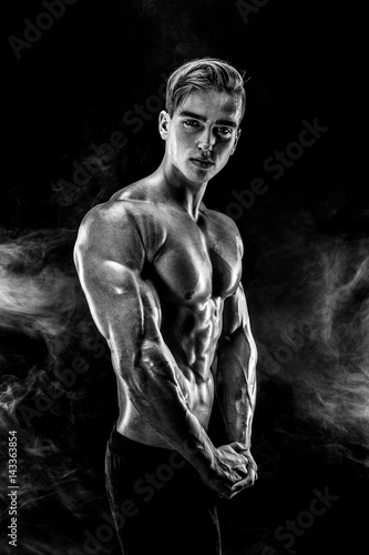 Strong Man Bodybuilder with Six Pack and perfect abs, shoulders, biceps, triceps and chest, personal fitness trainer flexing his muscles in smoke. photo