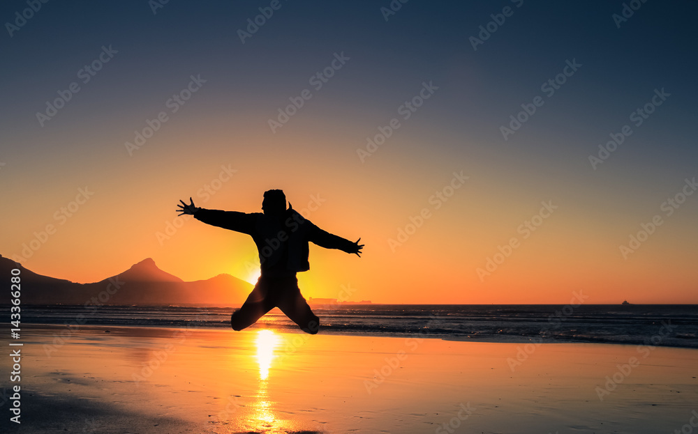 Silhouette of an young man jumping on the beach at Cape Town city, South Africa. Concept photo of happiness, freedom and lifestyle.
