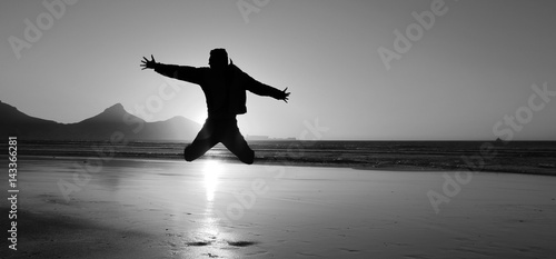 Silhouette of an young man jumping on the beach at Cape Town city, South Africa. Black and white picture.
