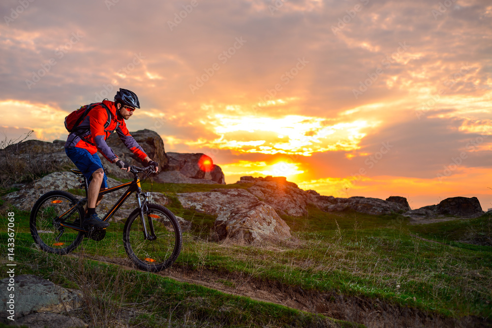Fototapeta premium Cyclist Riding Mountain Bike on the Spring Rocky Trail at Beautiful Sunset. Extreme Sports and Adventure Concept.