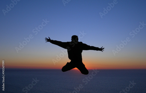 Silhouette of a man jumping in front of the sunset in the ocean. Concept photo of happiness, freedom and lifestyle.