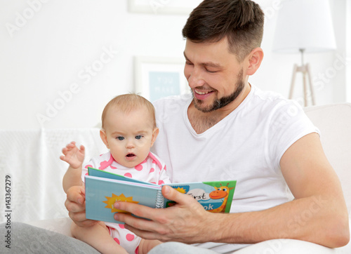 Father showing book to cute baby daughter at home