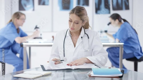Wallpaper Mural  Portrait smiling doctor sitting at desk with colleagues working in background Torontodigital.ca