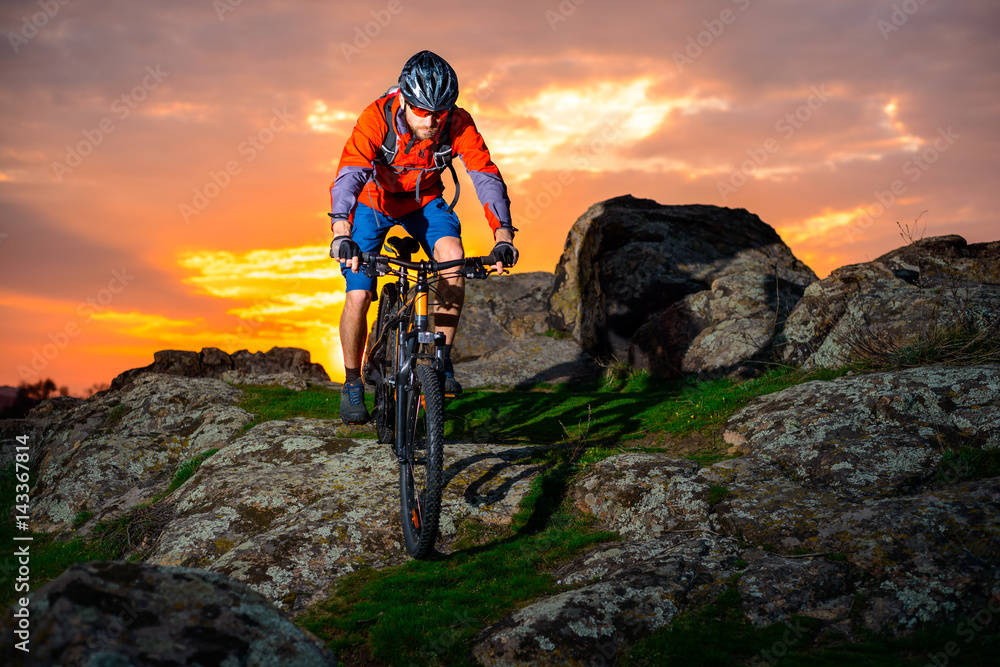 Fototapeta premium Cyclist Riding Mountain Bike Down Spring Rocky Hill at Beautiful Sunset. Extreme Sports and Adventure Concept.