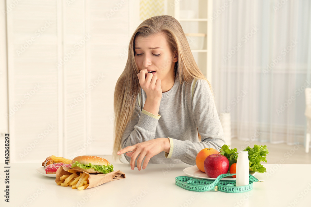 Beautiful young woman making choice between healthy and unhealthy food