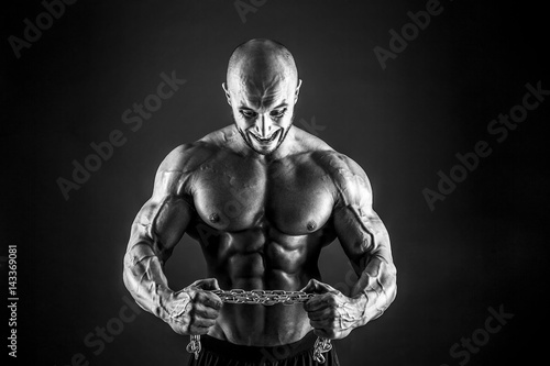 Portrait of aggressive bodybuilder trying to tear the metal chain. Isolated