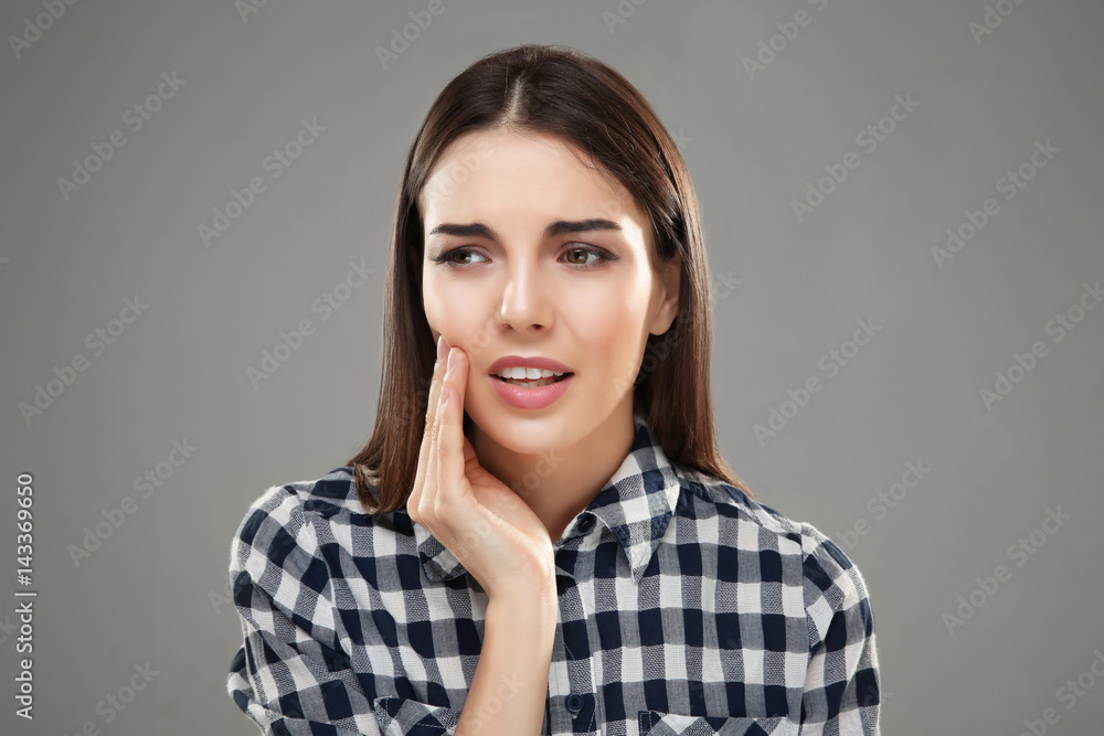 Beautiful young woman suffering from toothache on grey background