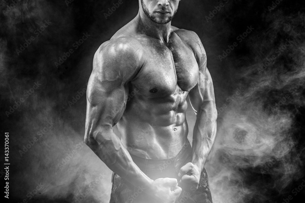 Strong bodybuilder with six pack, perfect abs, shoulders, biceps, triceps  and chest, personal fitness trainer flexing his muscles in smoke Stock  Photo