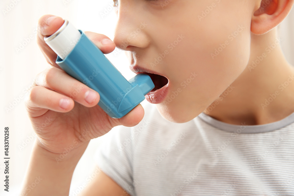 Fototapeta premium Boy using inhaler during asthmatic attack on light background, closeup