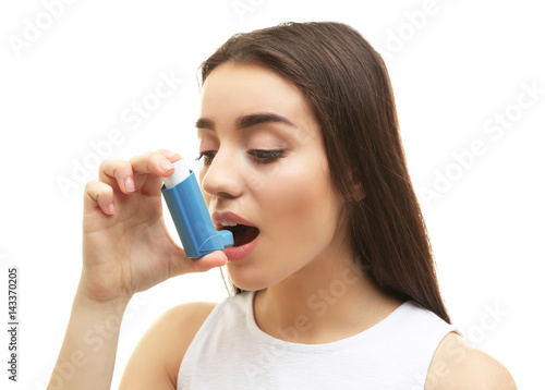 Young woman using inhaler during asthmatic attack, on white background