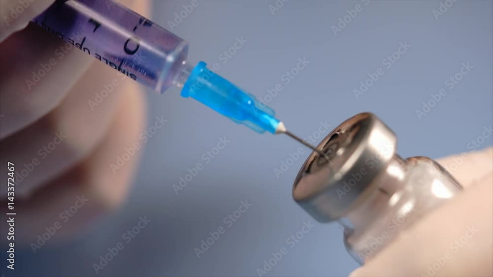 Close up syringe piercing the lid of the ampoule. Doctor's hands in white gloves Close up syringe piercing the lid of the ampoule. Doctor's hands in white gloves
