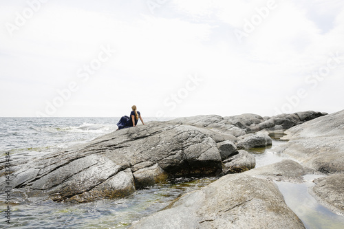 Sweden, Stockholm Archipelago, Sodermanland, Huvudskar, Mature woman sitting on rocky seashore photo