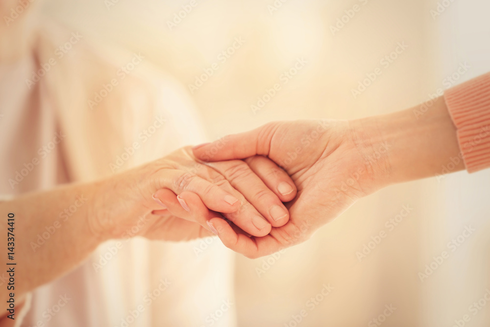 Old and young women holding hands on blurred background, closeup Old and young women holding hands on blurred background, closeup