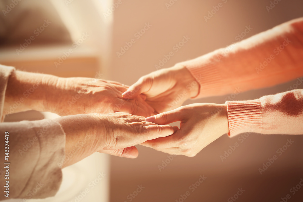 Naklejka premium Old and young women holding hands on blurred background, closeup
