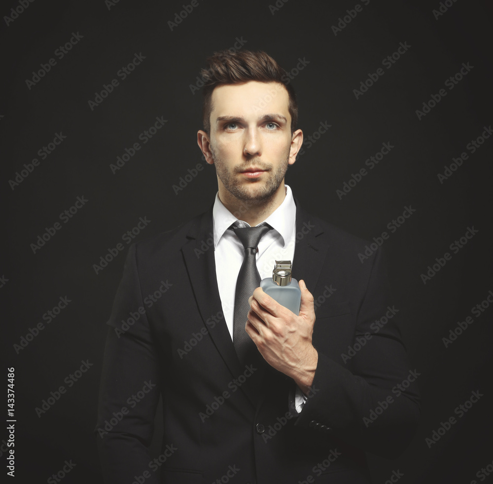Handsome young man using perfume on black background Handsome young man using perfume on black background