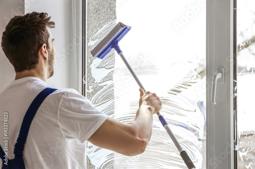 Young man washing window in...