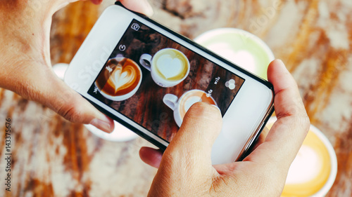 Woman using a smartphone taking a picture of a coffee in a cafe.