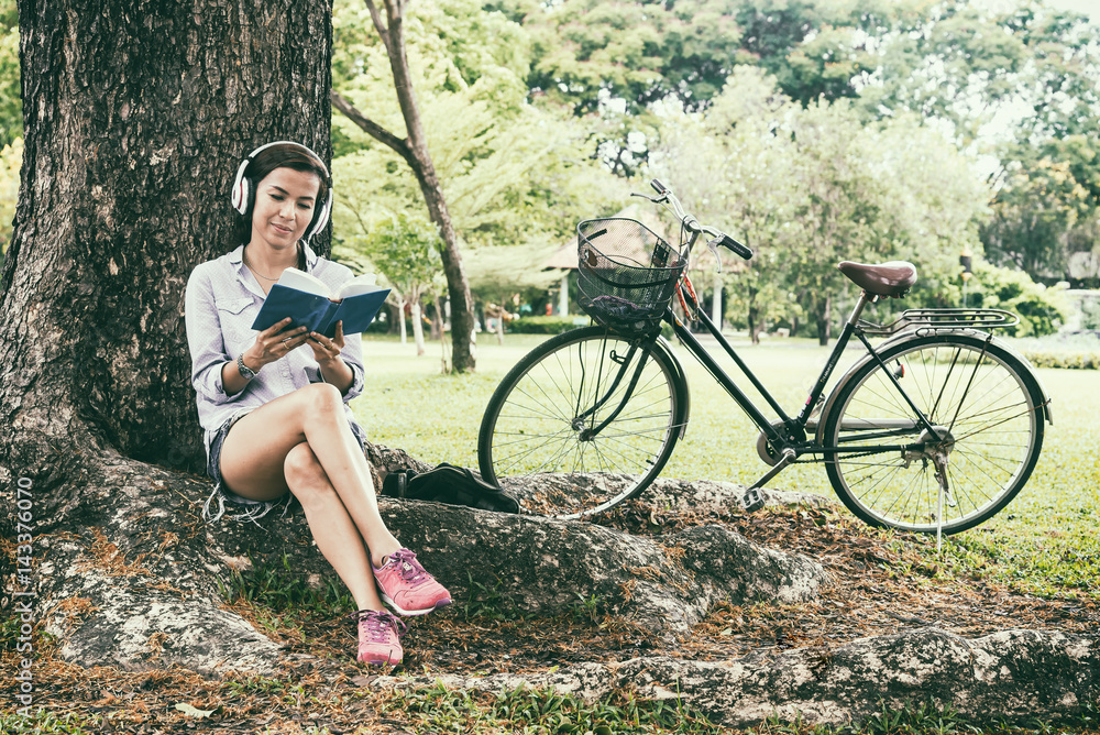 Woman reading a book while listening music in a park, vintage tone