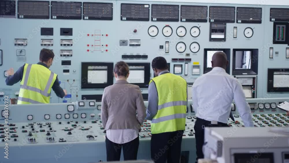 Workers in power plant control room looking at control panel & checking system