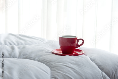 Fresh morning coffee in red cup on the bed.