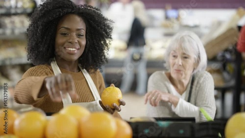  Friendly worker in a supermarket assisting senior lady buying groceries