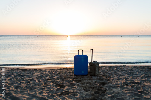 Two travel suitcases on sunrise sandy beach with sea background, summer holidays concept