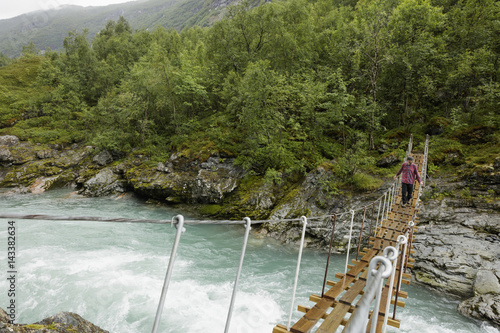 Norway, Jotunheimen, Utladalen, Man walking on suspension bridge over river photo