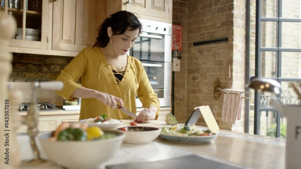 Woman preparing meal in kitchen at home & following recipe on computer tablet Woman preparing meal in kitchen at home & following recipe on computer tablet