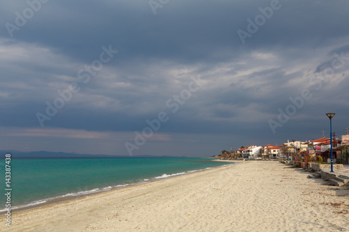 The village on the shore of the turquoise sea under a dark cloudy sky before the rain at sunset of the day.