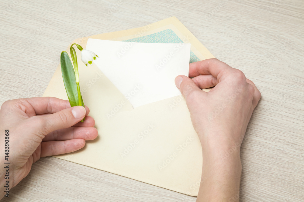 Hand holding a snowdrop flower and greeting card into the old envelope. Spring greetings. Hand holding a snowdrop flower and greeting card into the old envelope. Spring greetings.