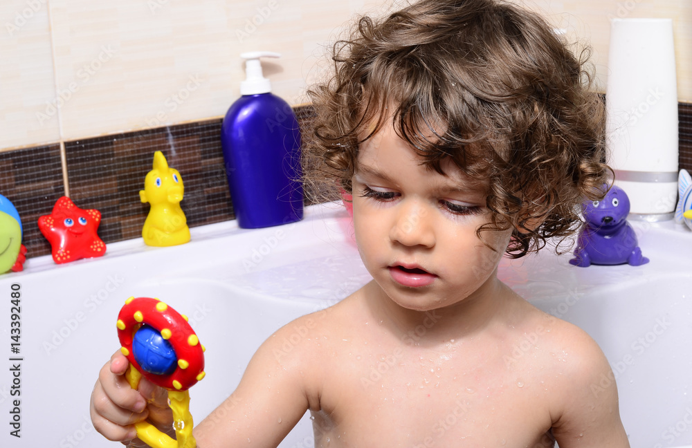 Beautiful toddler taking a bath in a bathtub with bubbles. Cute kid washing his hair with shampoo in the shower and splashing water everywhere. Boy playing with toys in the tub Beautiful toddler taking a bath in a bathtub with bubbles. Cute kid washing his hair with shampoo in the shower and splashing water everywhere. Boy playing with toys in the tub