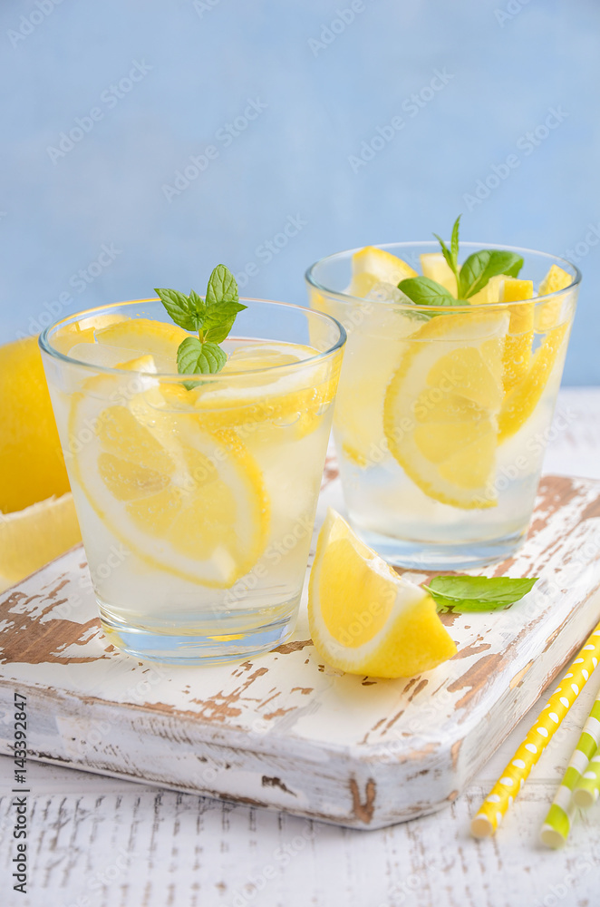Fototapeta premium Cold refreshing summer drink with lemon and mint on wooden background. Selective focus, copy space.