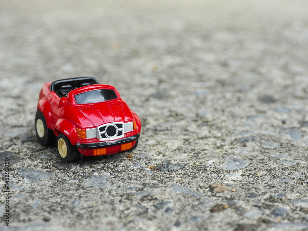 A red toy car park on rough cement road.