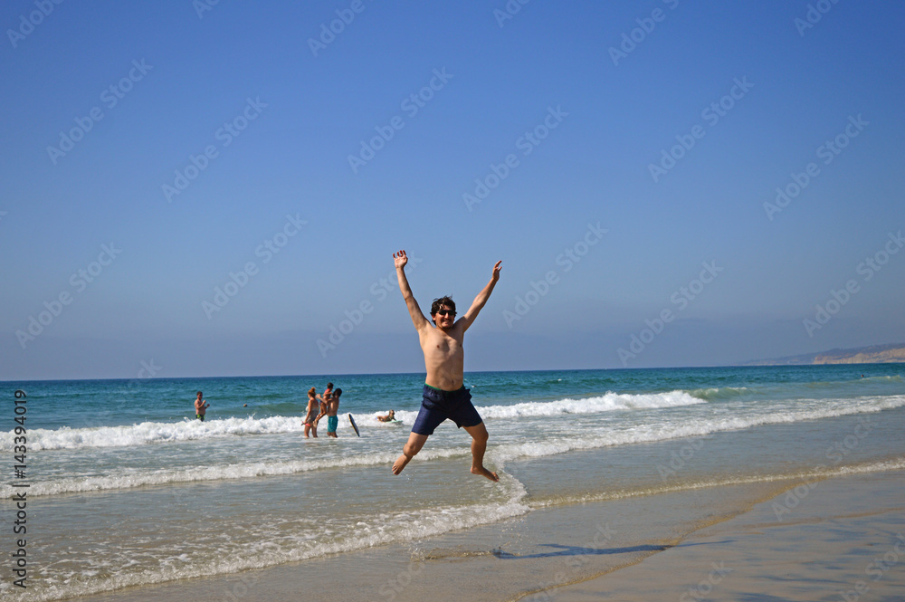 Happy tourist man jumping high on the beach and enjoying holiday in San Diego, California, USA