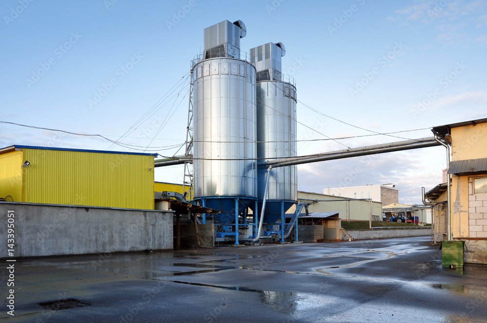 Obraz premium Buildings of woodworking factory plant. Metallic tanks with communication pipe and tower.