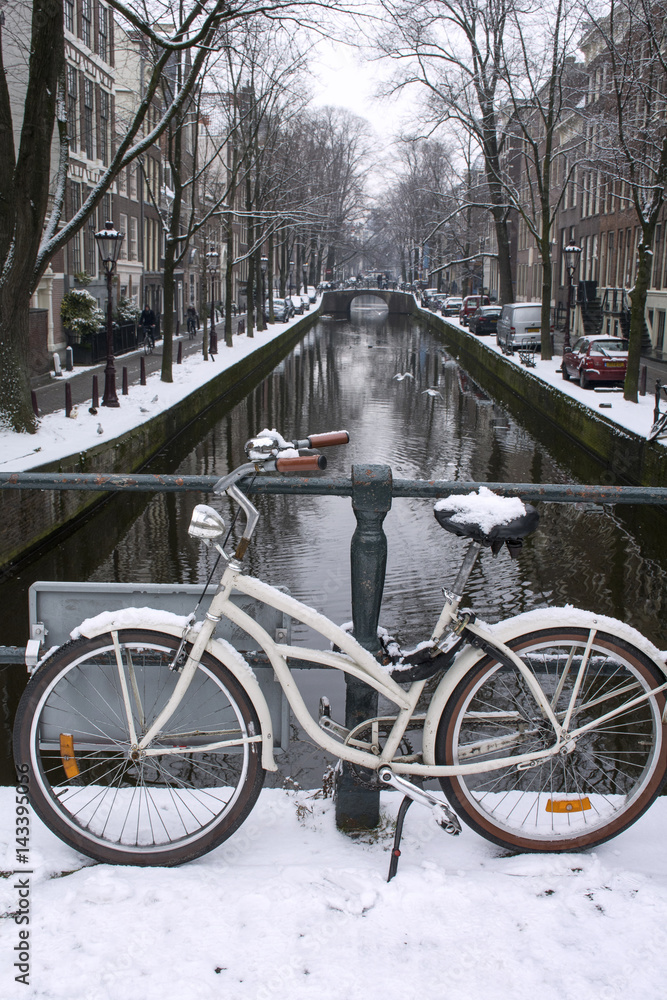 White bike with brown wheels in snow in winter near the canal in Amsterdam