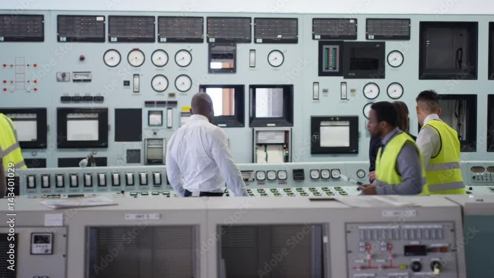 Workers in power plant control room looking at control panel & checking system