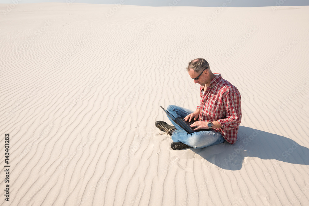 Man with a laptop sits alone in the middle of the desert