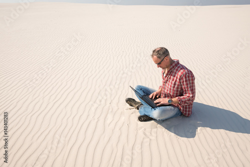 Obraz na płótnie Man with a laptop sits alone in the middle of the desert w salonie