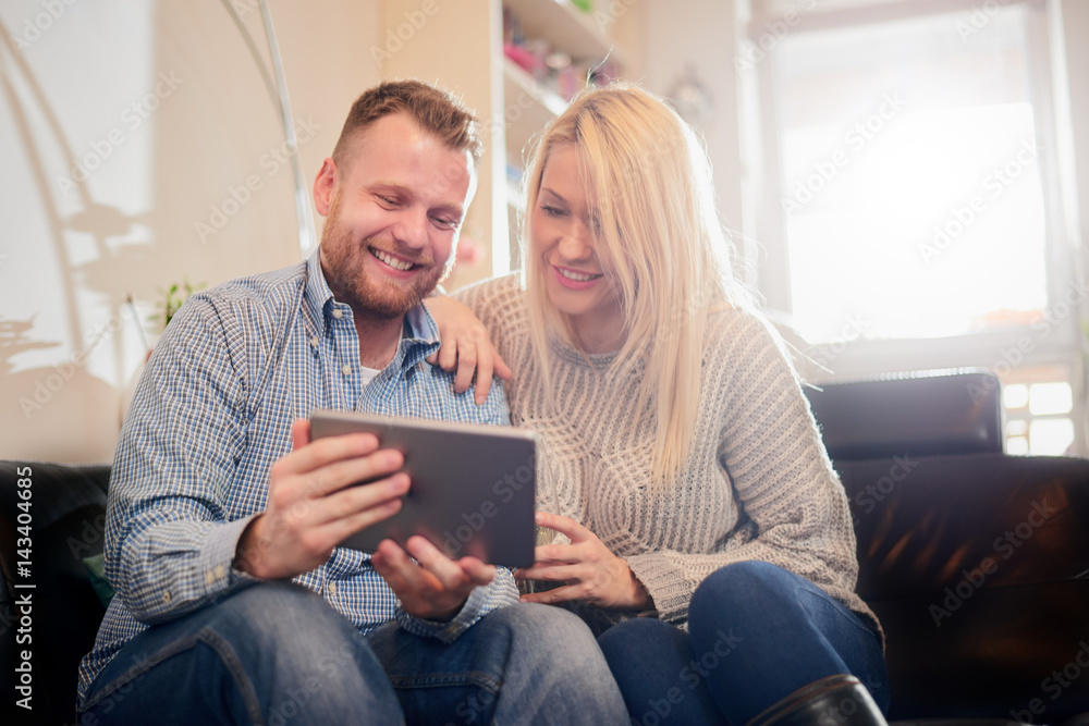 Happy couple smiling and sitting on sofa in living room. They using tablet
