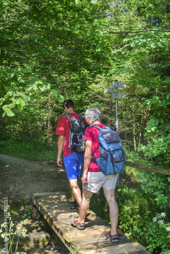 Zwei Wanderer überqueren einen kleinen Steg im Wald
