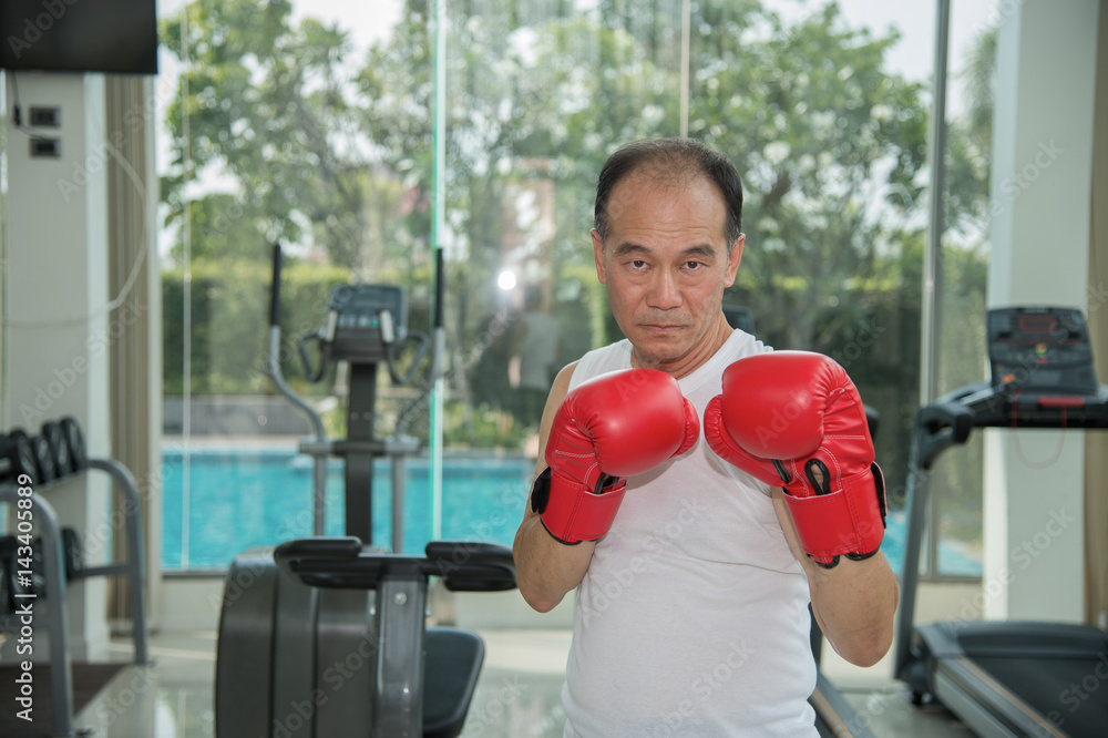 Old man wearing red boxing gloves exercising in fitness look to camera, ready to fighting, copy space for text
