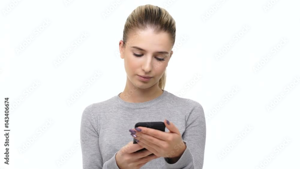 Unhappy frowning young woman typing message on smartphone over white background Unhappy frowning young woman typing message on smartphone over white background