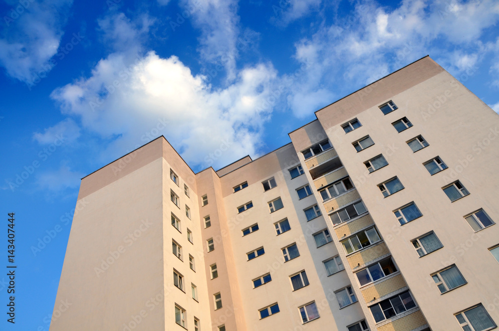 Looking up at the facade of of multistory apartment house on a background of blue sky with clouds.