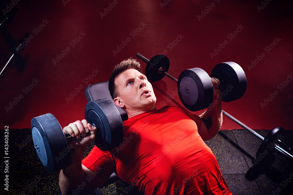 A sporty blond man doing exercises with dumbbells in the gym. A sporty blond man doing exercises with dumbbells in the gym.