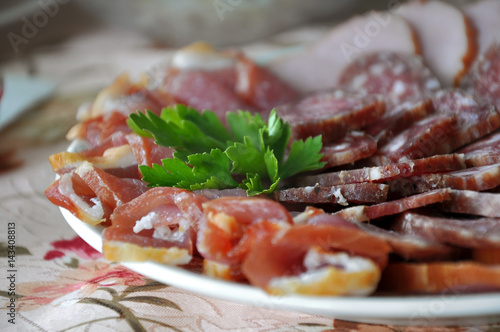 Different smoked sausages and meat decorated with parsley on a plate on a festive table close up.