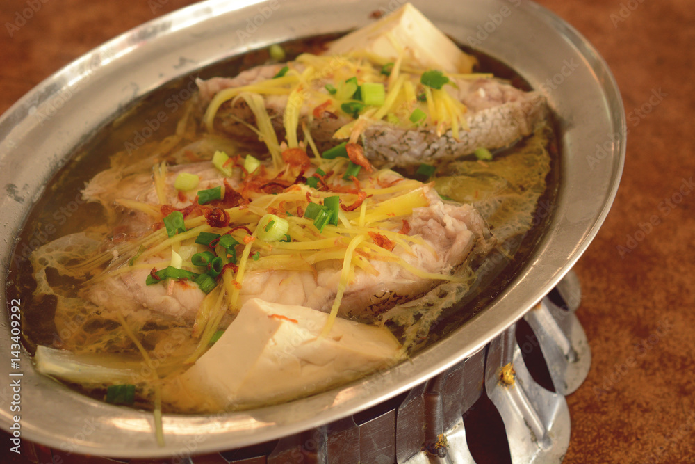 steamed grouper with ginger, tofu and chinese soy sauce served on hot pot.
