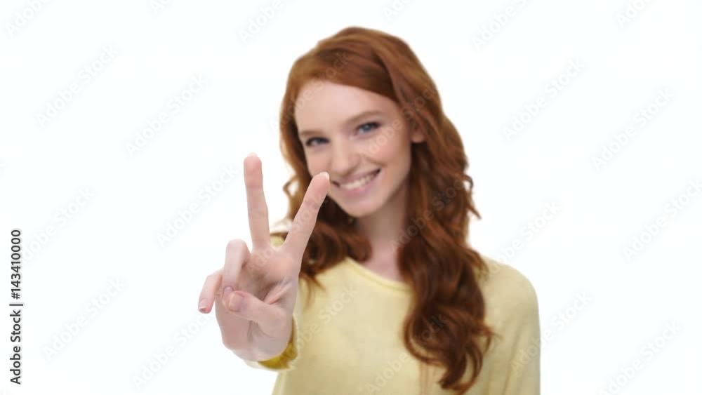 Cheerful attractive girl with long red hair showing peace gesture isolated over white Cheerful attractive girl with long red hair showing peace gesture isolated over white