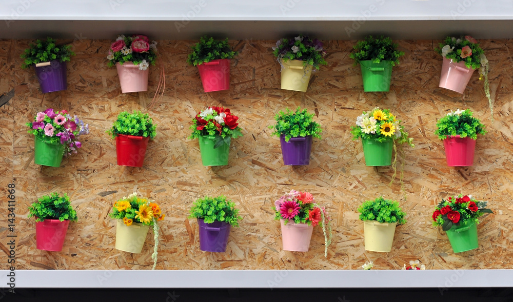 A lot of colored pots with flowers on a cork wall.