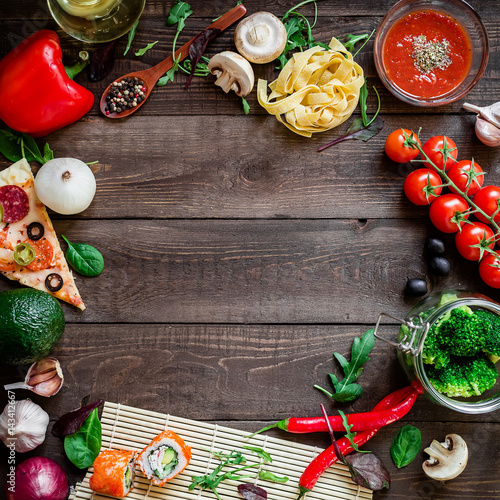 Food frame made of vegetables, pizza, sushi rolls, pasta and sauce on wooden background. Flat lay.